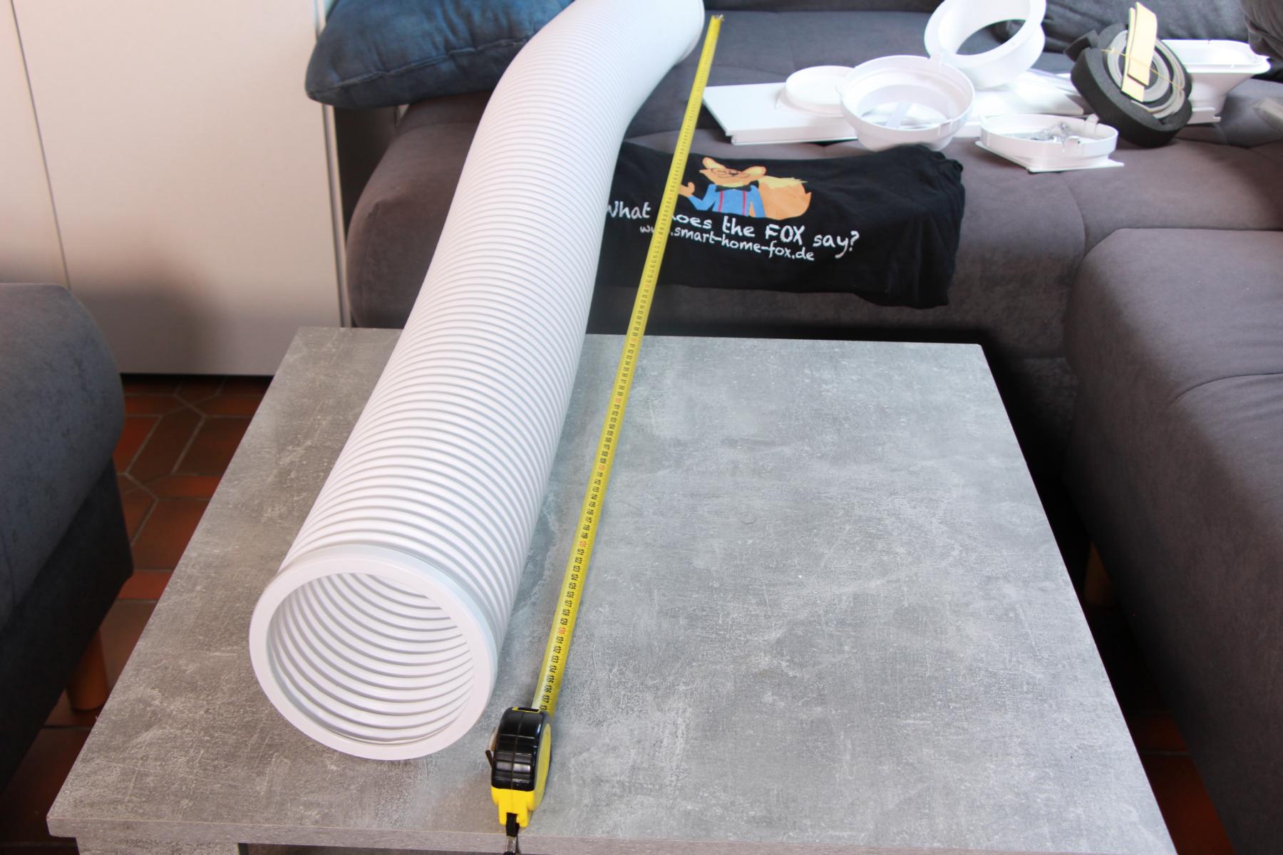 Der Abluftschlauch einer mobilen Klimaanlage ist ausgezogen und ausgebreitet und ein Maßband liegt daneben.